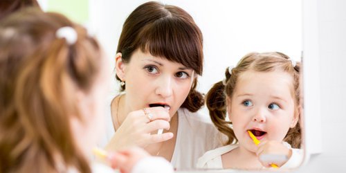 Mother persuade her daughter to brush her teeth to make good habit